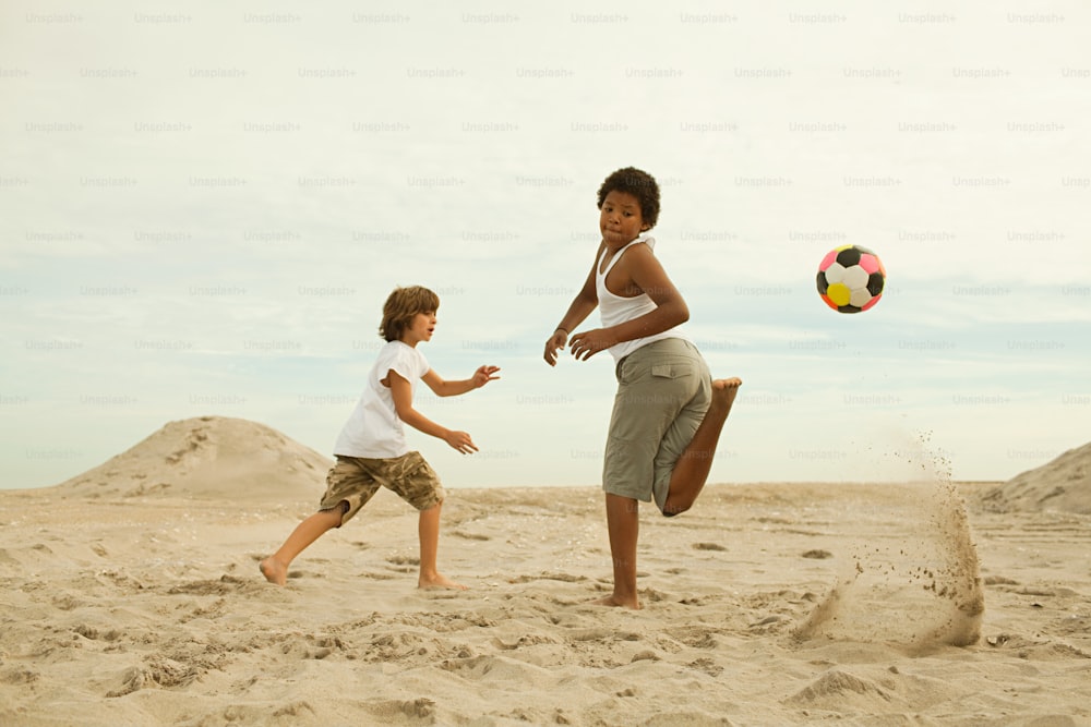 two children playing with a soccer ball in the sand