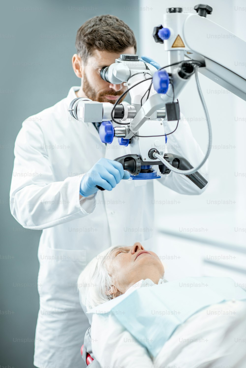外科歯科医院で専門の顕微鏡で歯を見ている年配の女性を診察する男性歯科医
