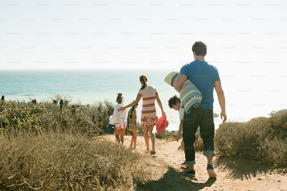 a group of people walking down a dirt road next to the ocean