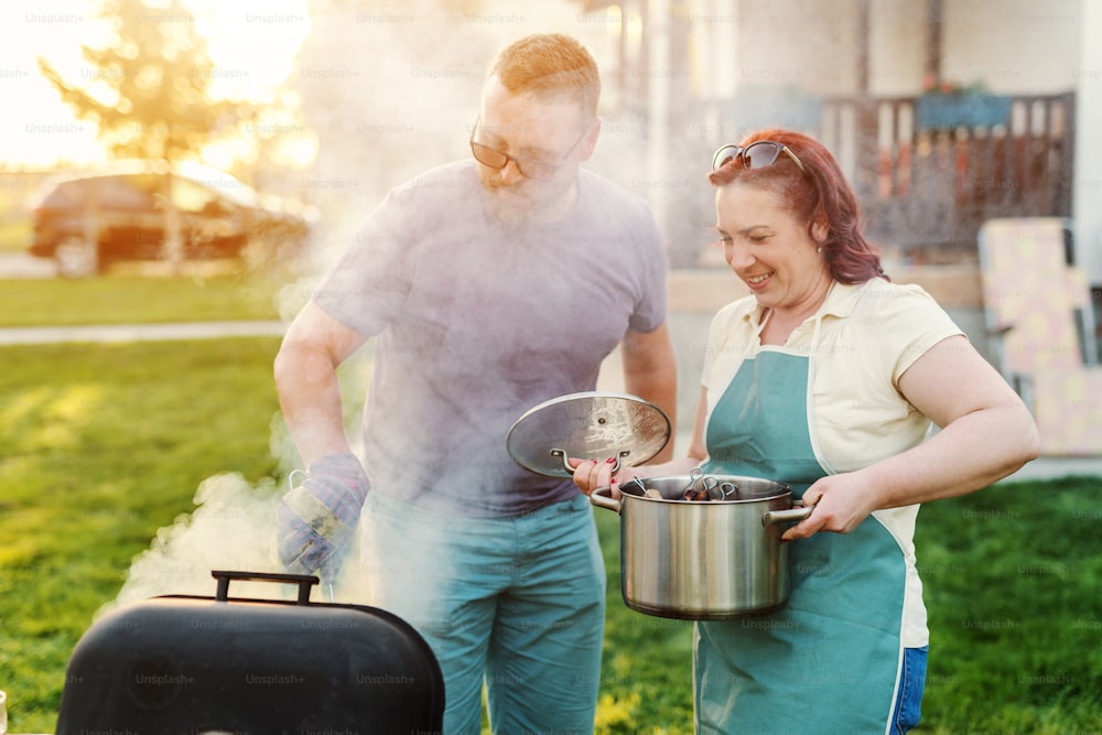 뒷마당에서 구운 고기를 준비하는 남편과 아내. 냄비를 들고 있는 여자. 가족 모임 개념.