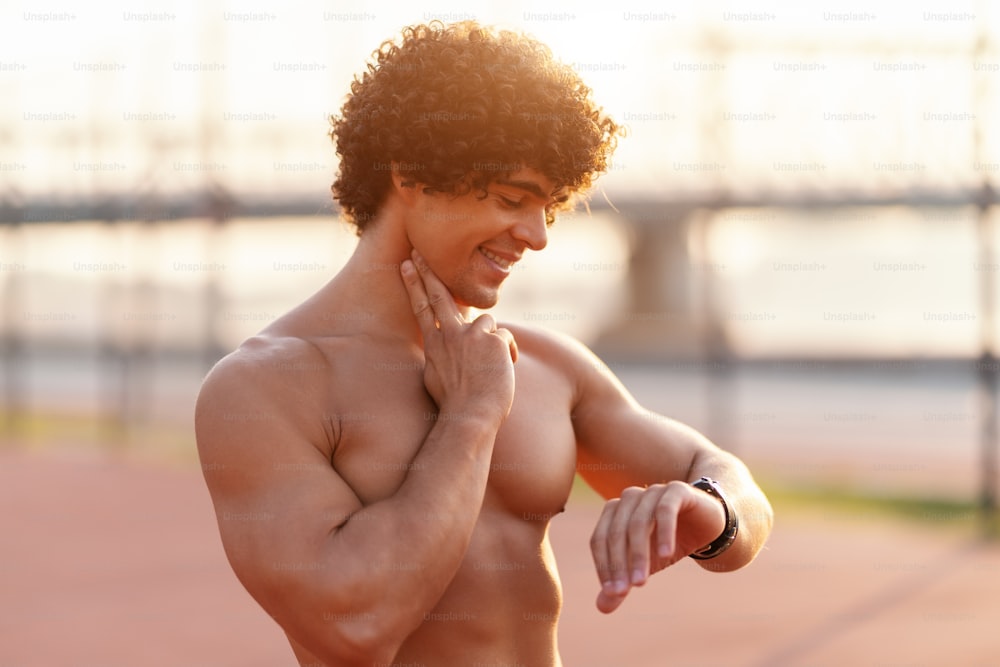 Close up of shirtless smiling sporty man checking heart beat after running. Morning time.