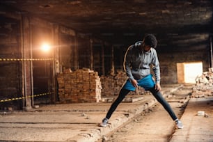 Homme sportif afro-américain en vêtements de sport étirant les jambes dans une vieille usine de briques. Concept de mode de vie sain.