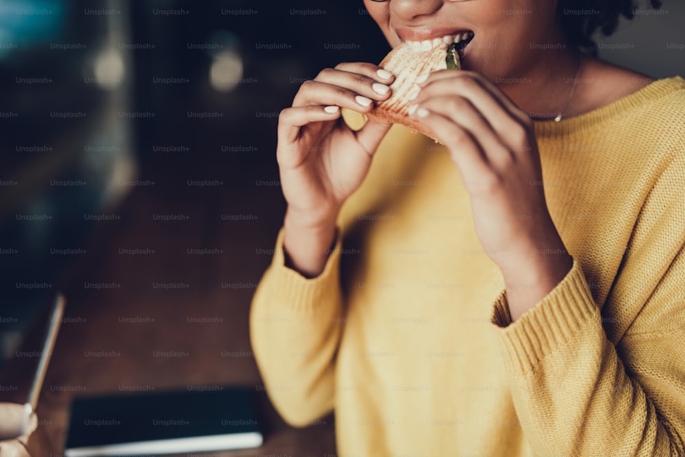 Cropped photo of attractive lady with food. She eating best sandwich in cafe and smiling