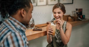 Hermosa chica de la generación z sonriendo con un café helado en la mano en la barra del bar de una cafetería de moda con un chico de raza mixta