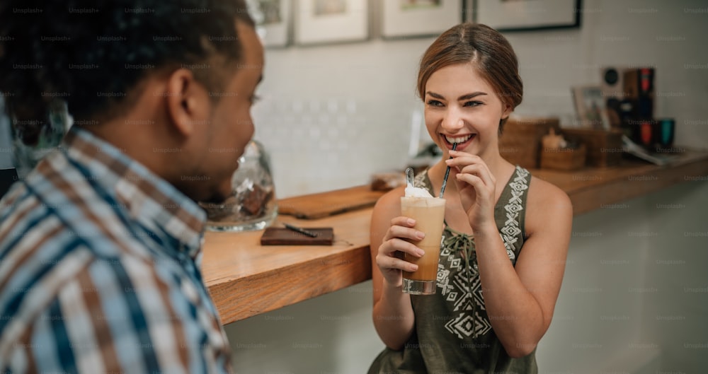 Beautiful generation z girl smiling with a iced coffee in hand at bar counter of a trendy coffee shop with mixed race guy