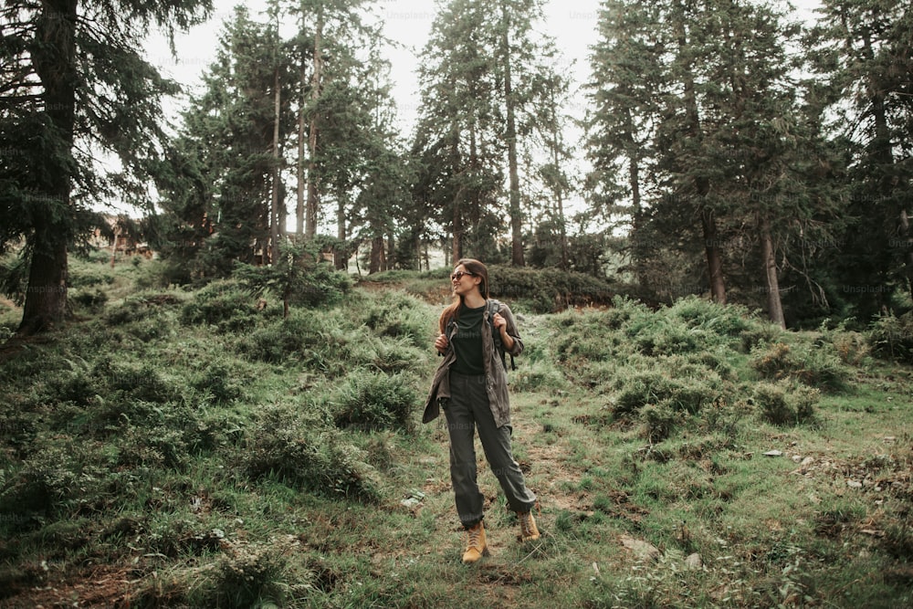 Splendid nature. Full length portrait of young woman enjoying hike in coniferous wood. She is looking away and smiling