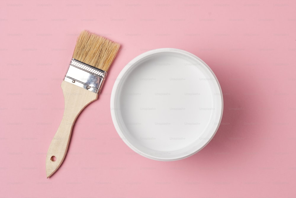 Brush and paint can with white color on yellow background, top view