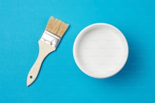 Brush and paint can with white color on blue background, closeup