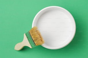 Brush and paint can with white color on green background, top view
