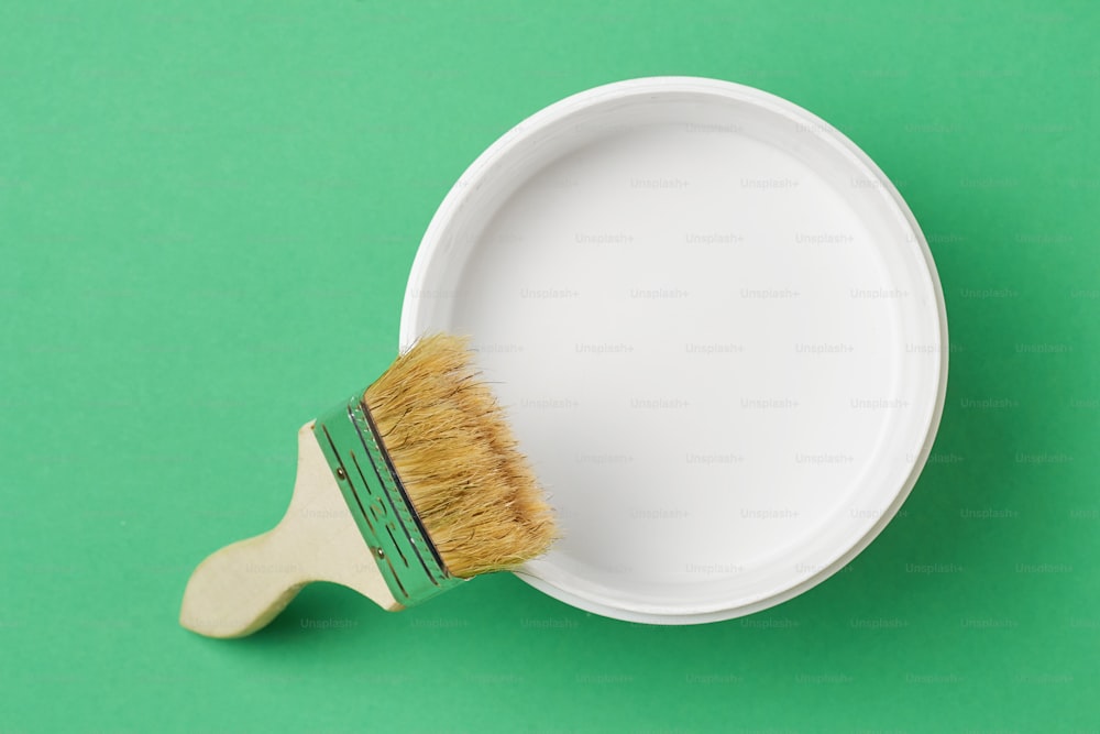 Brush and paint can with white color on green background, top view