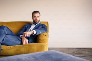 Sentirse relajado... El hombre de negocios guapo y bien vestido descansa en el sofá y piensa en los negocios. Look de moda. Concepto de negocio.