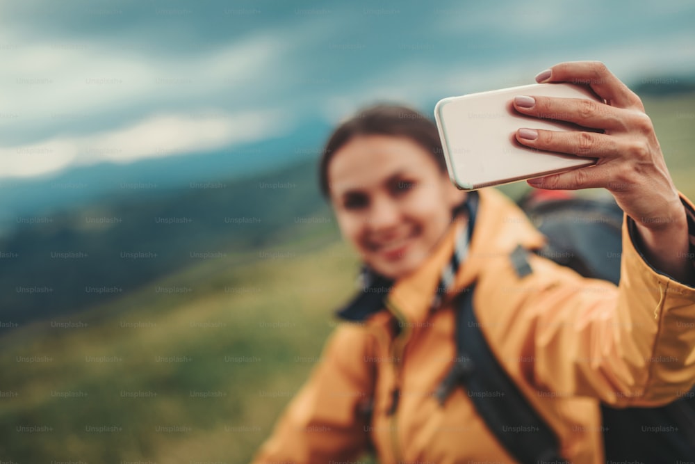 Nahaufnahme eines Smartphones in den Händen einer schönen jungen Frau, die Fotos macht und sich auf den Berghügeln ausruht