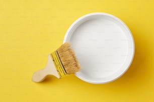 Brush and paint can with white color on yellow background, top view