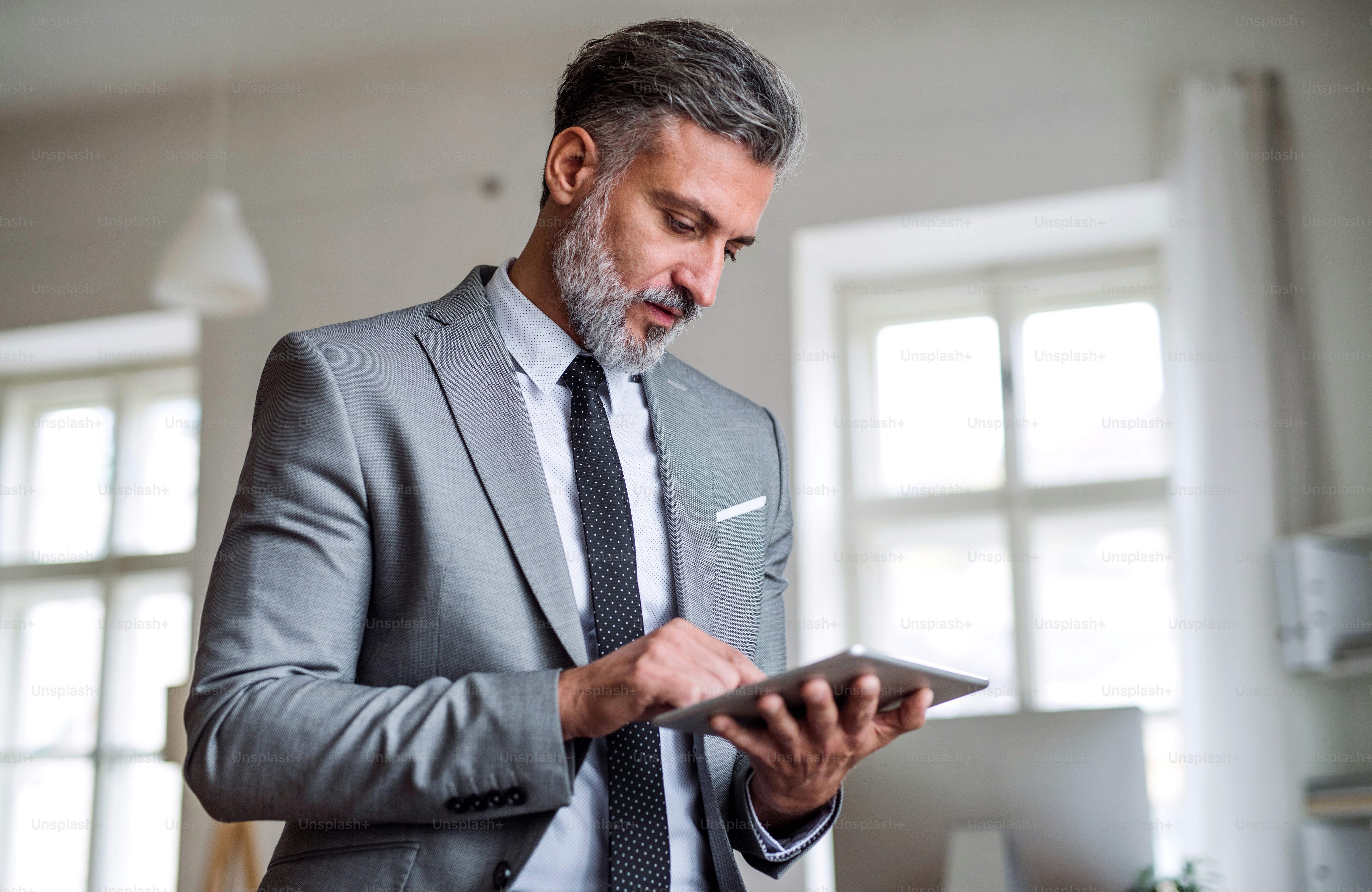 A waist-up portrait of mature businessman standing in an office, using tablet