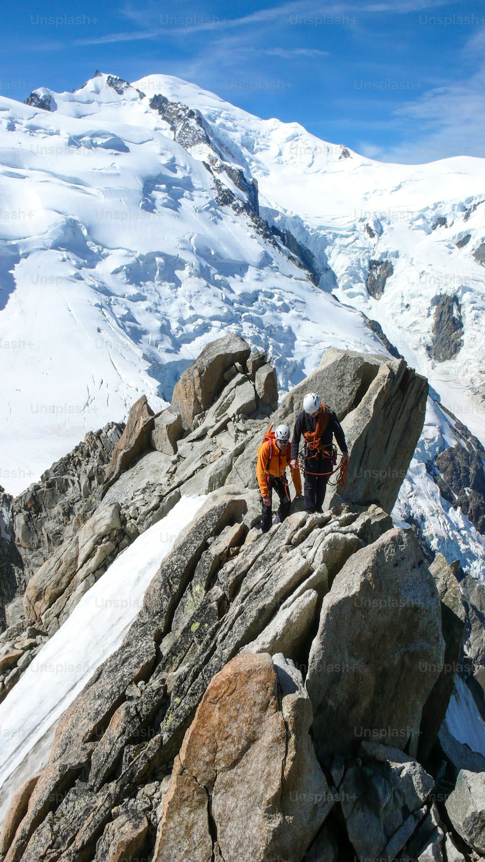 Bergführer und ein männlicher Kunde auf einem Fels- und Schneerücken auf dem Weg zu einem hohen Gipfel in den französischen Alpen bei Chamonix