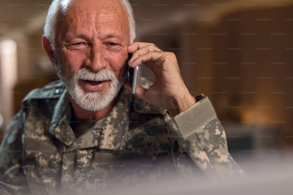 Soldato anziano sorridente che usa il telefono cellulare e parla con qualcuno in ufficio.