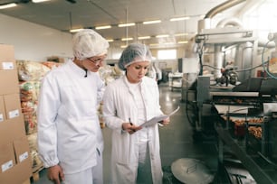 Due professionisti della qualità in uniformi sterili bianche che controllano la qualità dei bastoncini di sale mentre si trovano in una fabbrica alimentare.