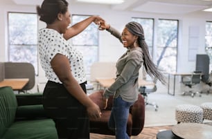 Two black african woman dancing and smiling. Friends greeting in a modern coworking space