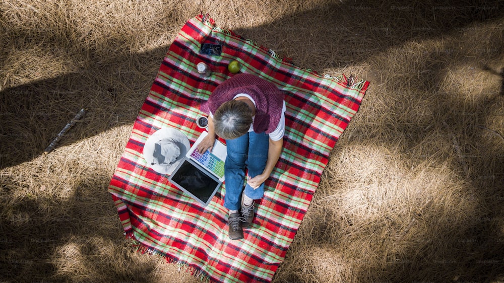 빨간 덮개에 숲에 앉아 기술 노트북 컴퓨터를 사용하여 위의 공중 꼭대기에서 본 한 여성 - 야외 여가를 즐기는 대안 독립 사람들을 위한 트레킹 등산객 개념