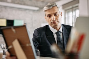 Mid adult businessman feeling sad while looking at photo in picture frame at work.
