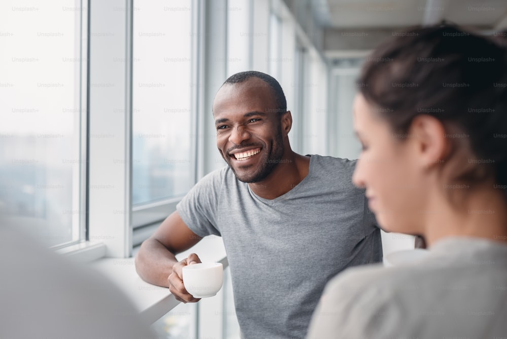 Happy African American employee have fun at coffee break in office, excited male worker laugh at colleague joke, multiracial co-workers smile negotiating. Teambuilding concept