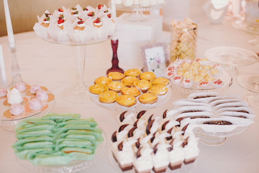 결혼식 피로연에서 테이블 파티에 맛있는 eclairs, 마카롱, 컵 케이크, 디저트 및 과자. 흰색과 분홍색 세련 된 캔디 바. 크리스마스와 새해 축제. 축하 및 파티