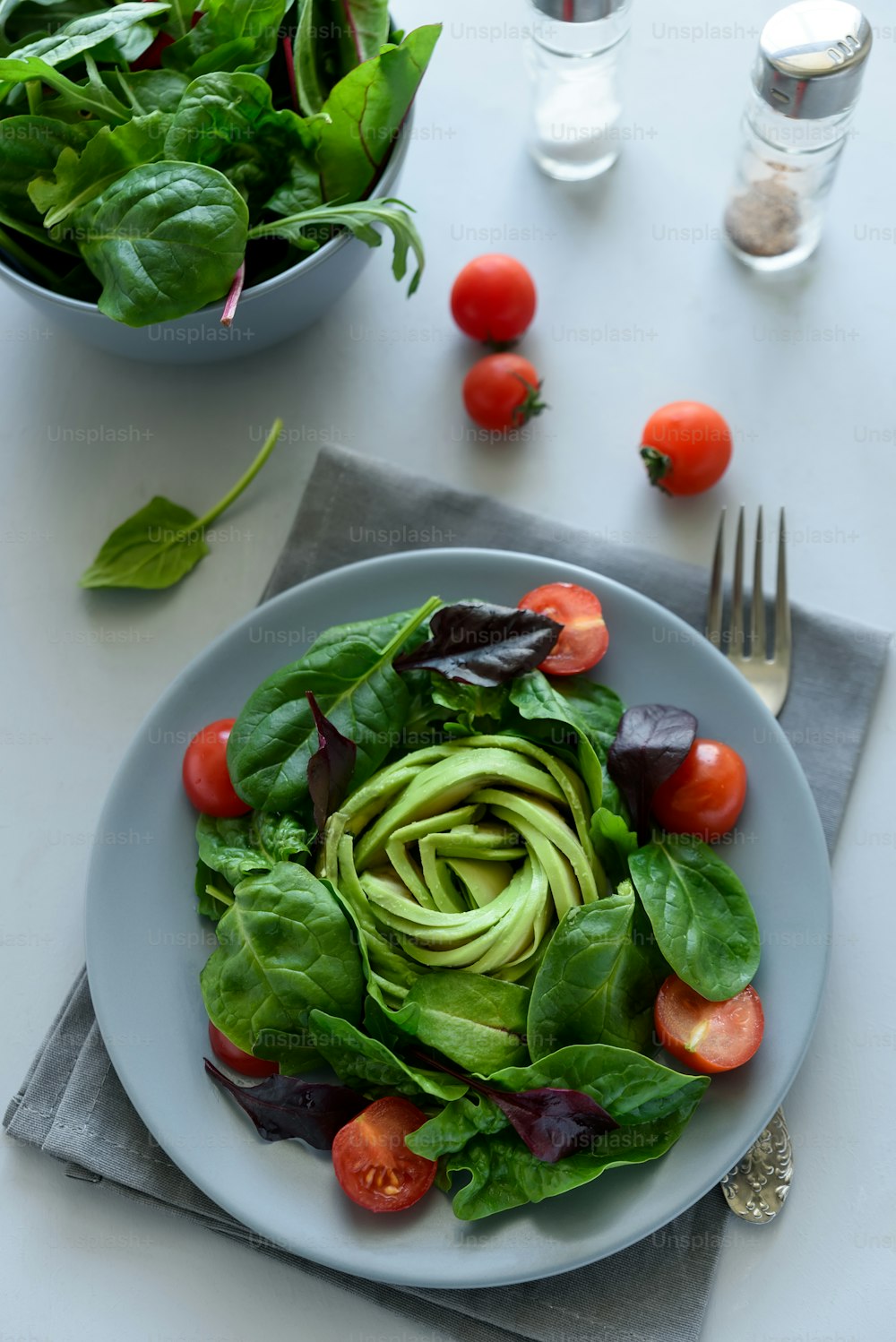 Mezcla de ensalada con aguacate, espinacas, tomates y hojas de remolacha sobre fondo de madera gris. Concepto de comida vegetariana. Enfoque selectivo.