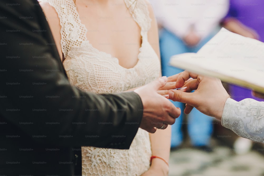 교회에서 거룩한 결혼식 동안 결혼 반지를 교환하는 행복한 세련된 결혼식 커플. 금반지를 끼고 있는 신랑 신부