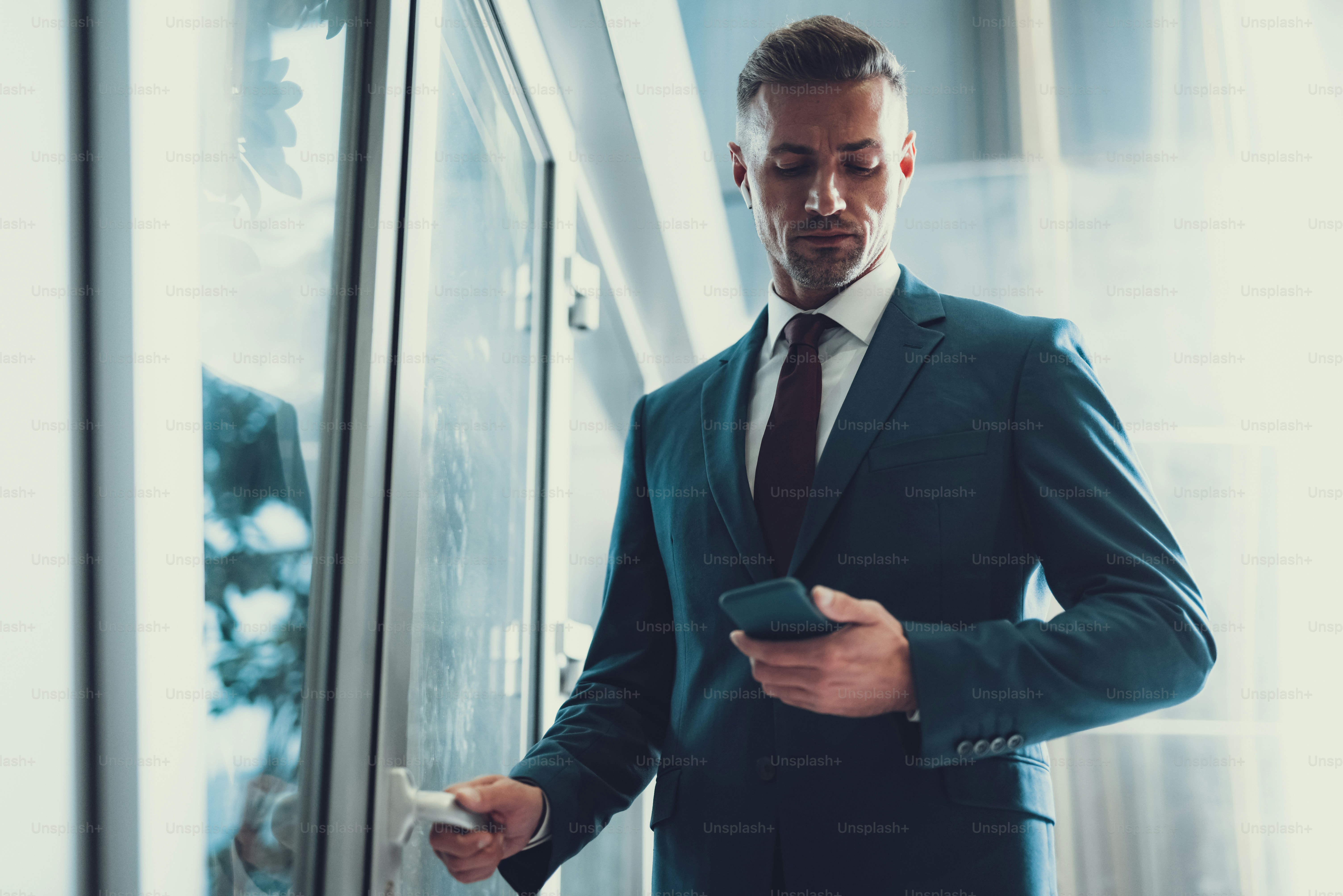 Low angle top view of good-wearing confident adult man looking at cellular screen. He opening door in office in business center