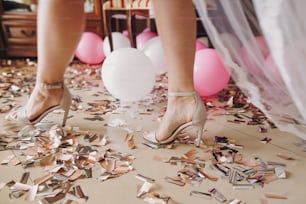 Mädchenbeine in stilvollen weißen Schuhen, die auf goldenem und silbernem Konfetti laufen, Brautboudoir-Morgendetails vor der Hochzeitszeremonie. Hühnerdusche. Weihnachts- und Neujahrsfeiern. Partei