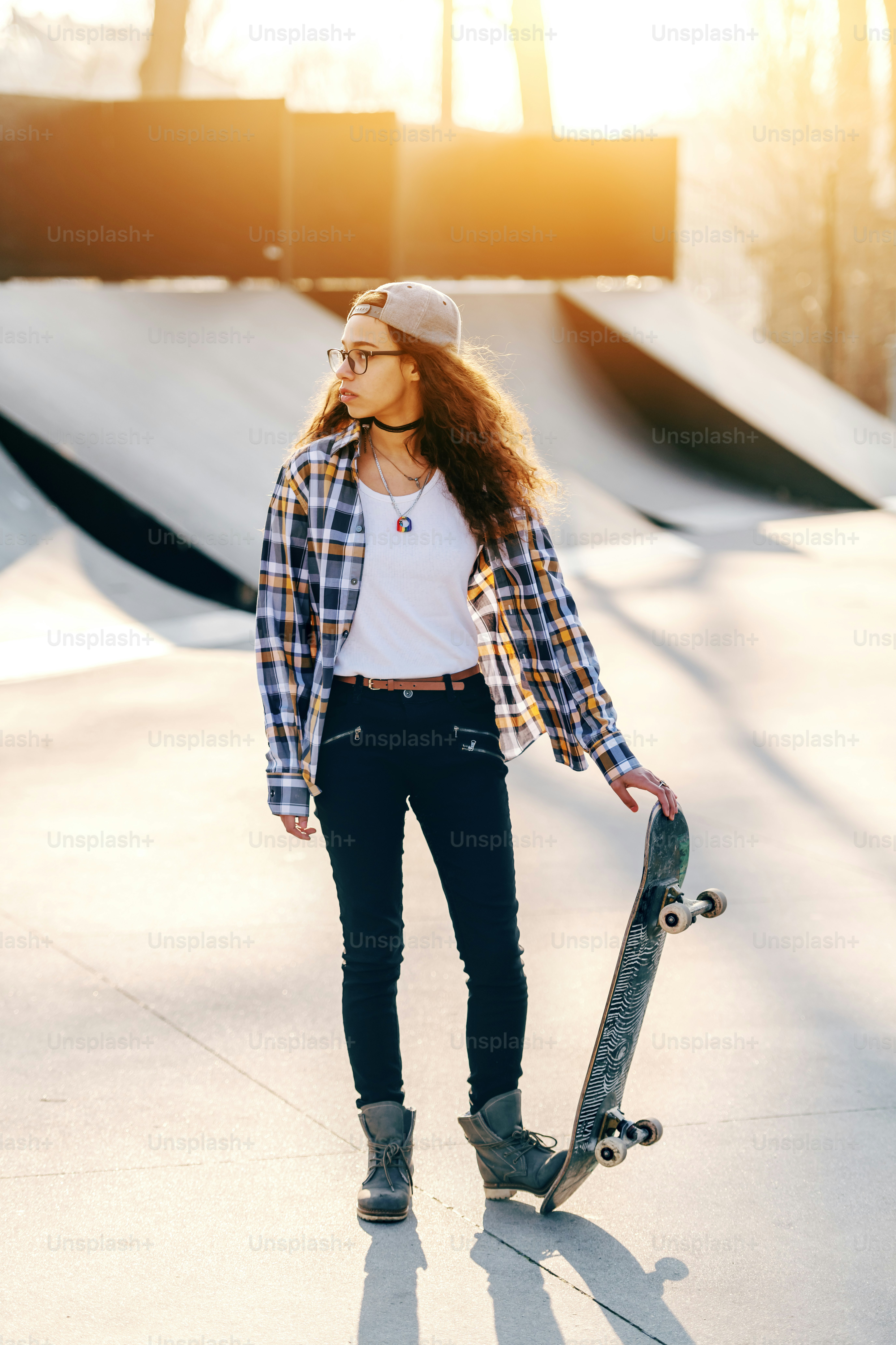 Belle adolescente urbaine métisse aux cheveux bouclés posant avec une planche à roulettes au skate park.