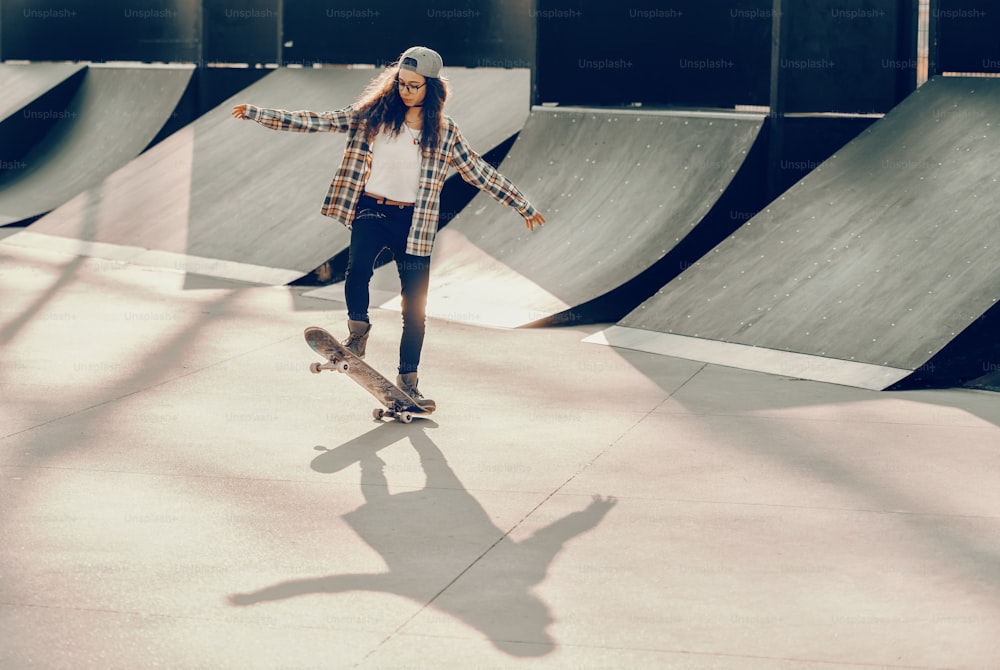 Cute mixed race teenage girl with curly hair and cap riding skateboard at skate park.