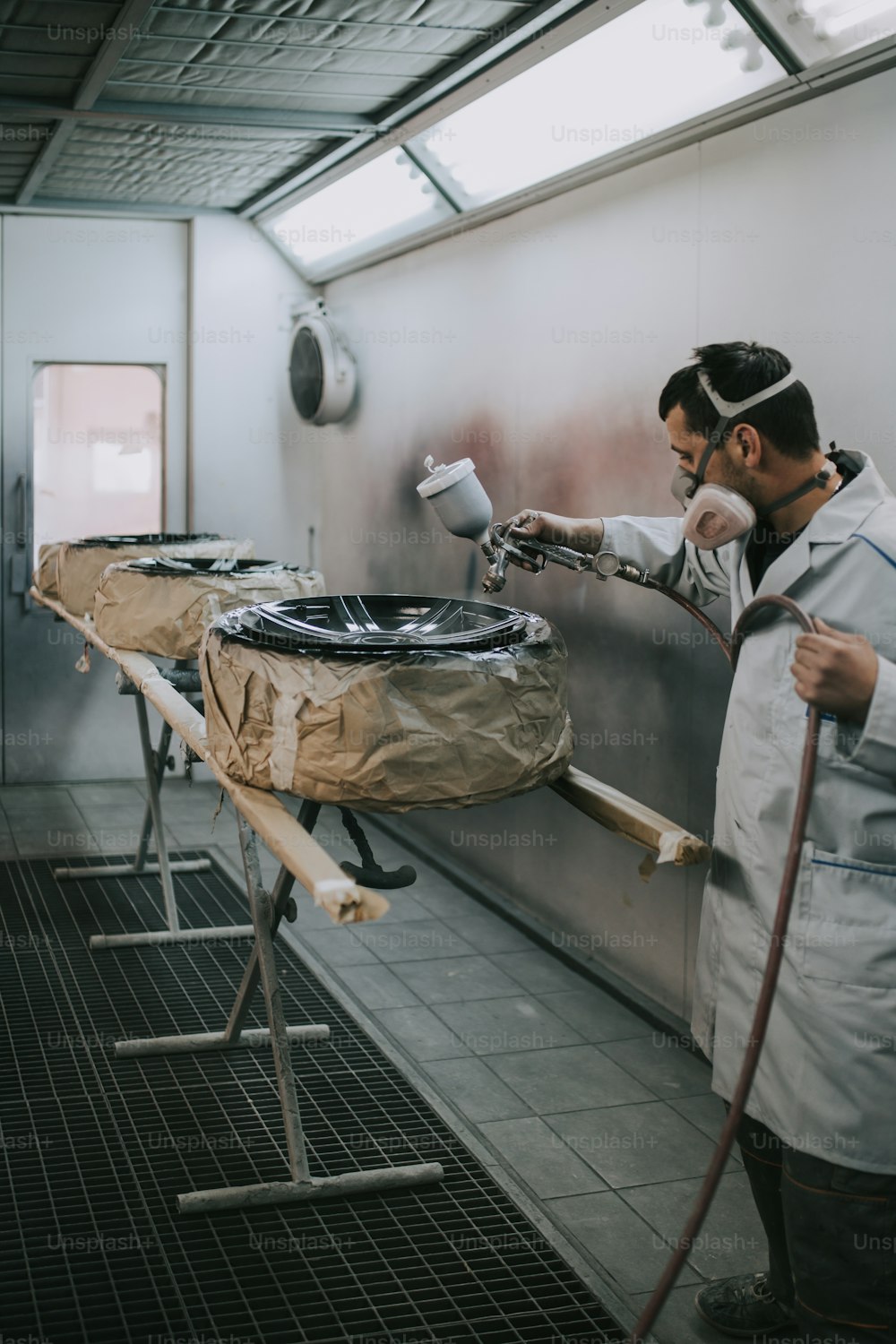 Man with protective clothes and mask painting car parts using spray compressor. Selective focus.