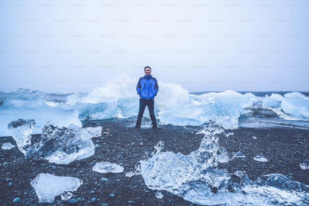젊은 남자 여행자는 아이슬란드의 다이아몬드 비치로 여행합니다. 유럽 아이슬란드 남동부 바트나요쿨 국립공원의 아름다운 빙하 석호에서 흘러나오는 것으로 알려진 검은 모래 해변의 얼어붙은 얼음.