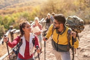 Group of happy hikers walking on the glade and chatting. In foreground couple leading the group. Autumn time.