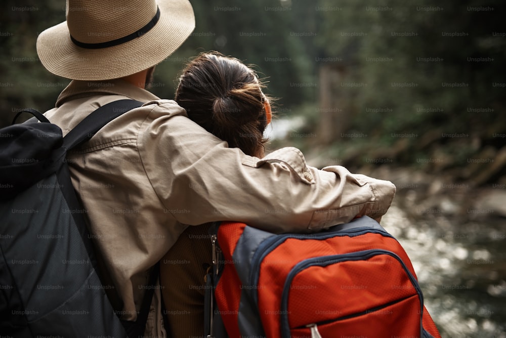 Hugging. Caring kind man wearing big hat and gently hugging his girlfriend while looking at the mountain river with her