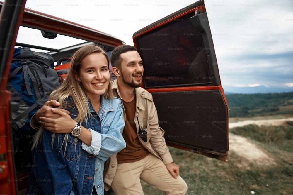 Positive young loving couple enjoying view of Carpathian mountain hills while sitting in their off-road car