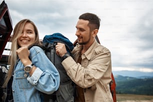 Delighted smiling young woman wearing a backpack with her boyfriend while resting outdoors