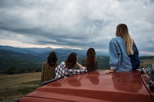 Active teambuilding. Rear view of a group of young travelers standing near their vehicle while traveling in the mountains
