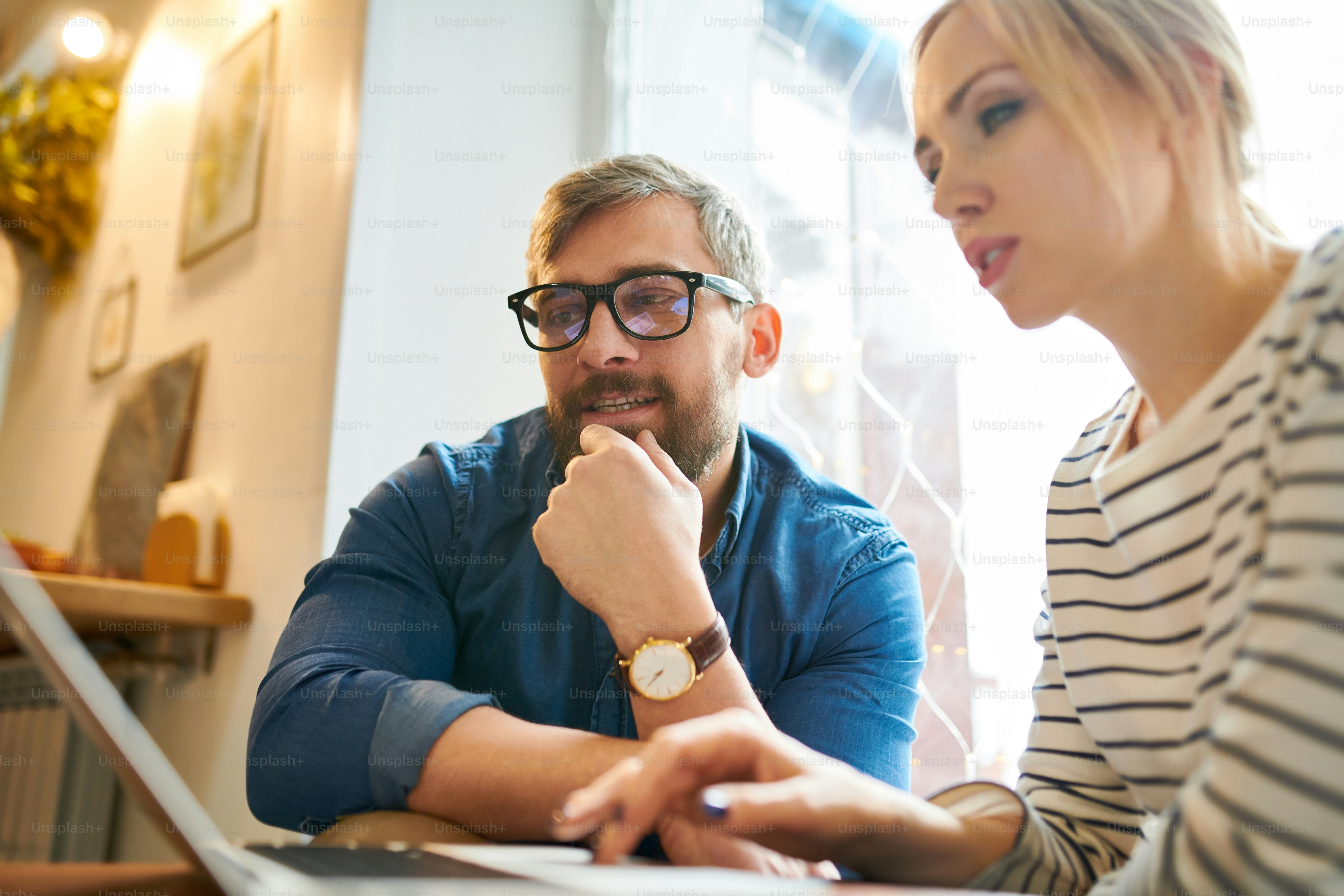 Contemporary young woman and man in casualwear looking at laptop display while searching for online data
