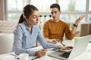 Giovane donna d'affari che fa acquisti su Internet con carta di credito e ignora il suo collega maschio in ufficio.