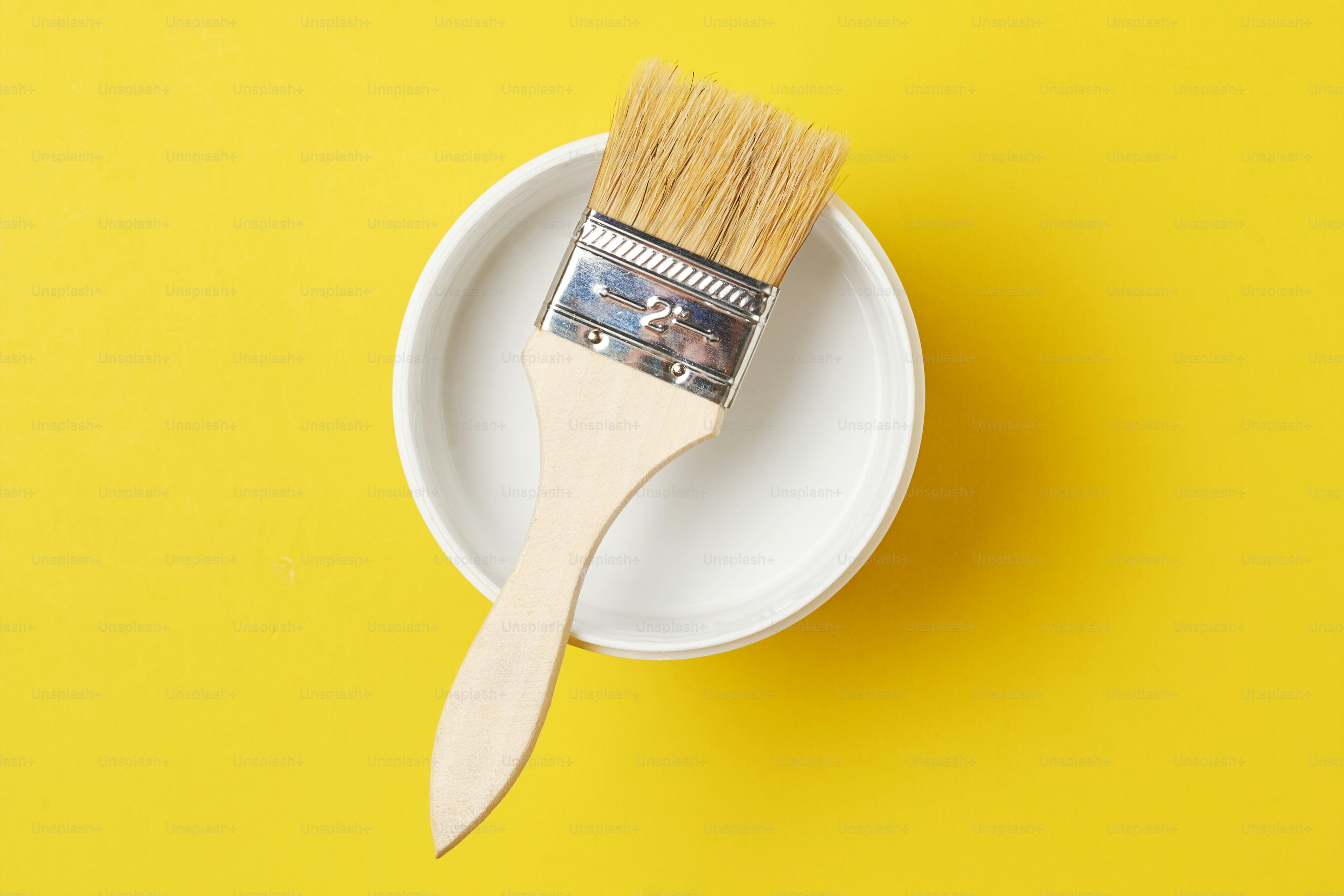Brush and paint can with white color on yellow background, top view
