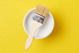 Brush and paint can with white color on yellow background, top view