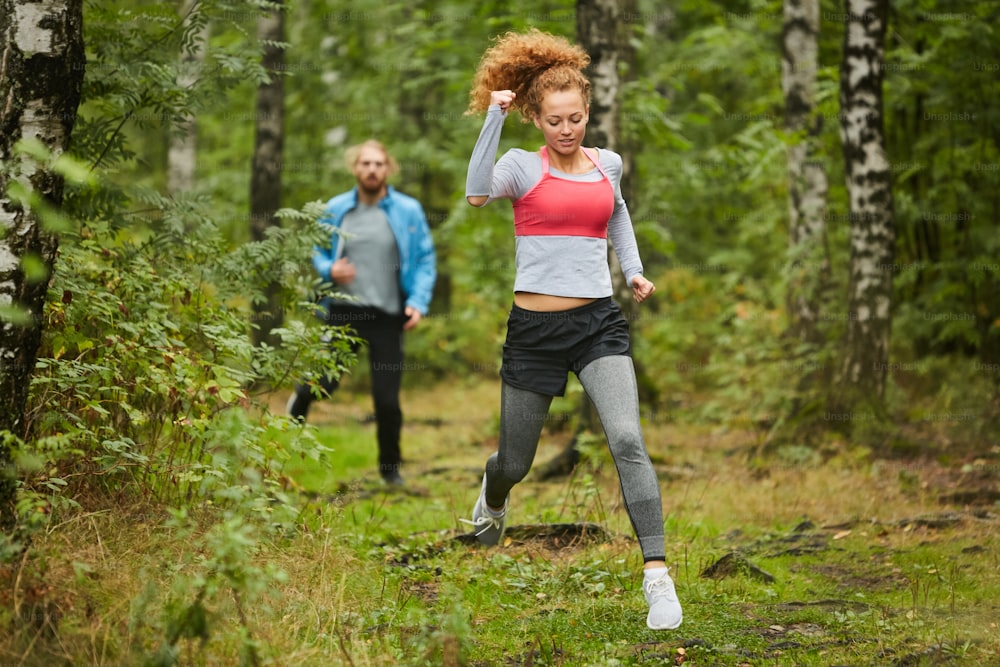 Joven pareja activa en ropa deportiva corriendo en el entorno natural en la mañana de verano antes del entrenamiento