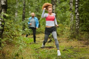 Young active couple in sportswear running in natural environment on summer morning before workout