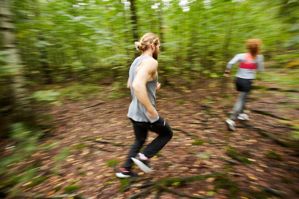 Giovane attivo che corre dietro la sua ragazza mentre si muove lungo il sentiero della foresta tra betulle sfocate