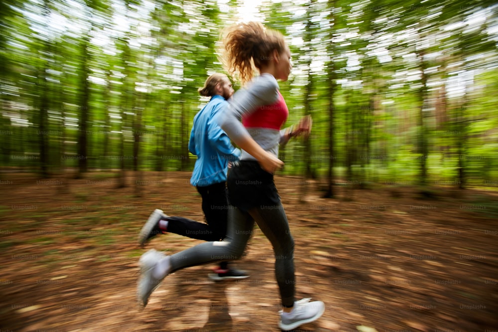 Giovane coppia in abbigliamento sportivo che corre sulla strada forestale con alberi sfocati sullo sfondo