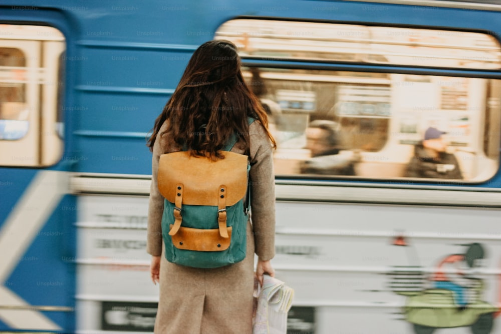 電車の前の地下鉄駅でバックパックと地図を持つ若い女性巻き毛の赤い頭の女の子の旅行者