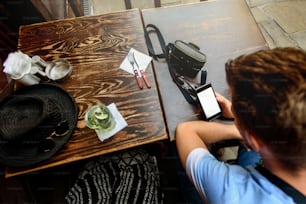 맛있는 모히토와 사진 카메라가 있는 나무 테이블에 빈 화면이 있는 전화기를 들고 있는 여행자 남자, 여름 휴가 개념