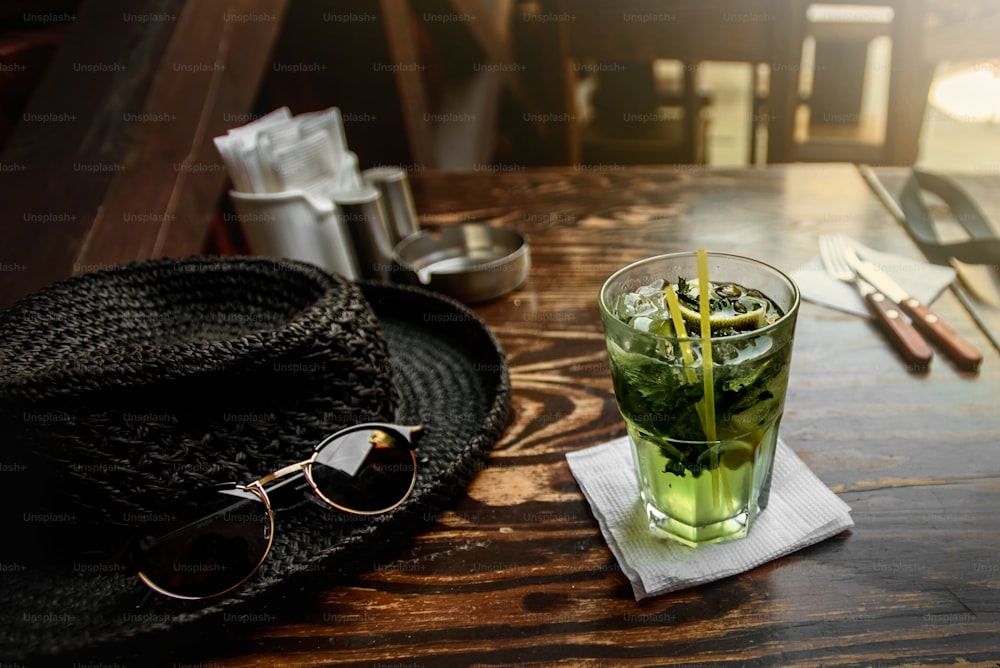 tasty mojito on wooden table with hat and sunglasses at restraunt, summer vacation concept